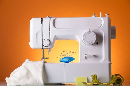 Sewing machine, fabric under sewing foot, pillow with needles and centimeter, on bright orange backgroundの写真素材