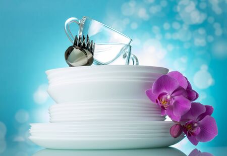Stack of clean plates, cups, spoons and forks on light blue backgroundの写真素材