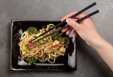 Spicy Asian dish, noodles with meat and vegetables with sesame, on black ceramic plateの写真素材