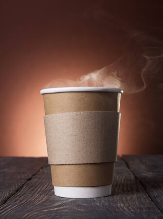 Disposable Cup of steaming hot coffee on dark wooden tableの写真素材