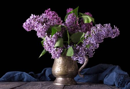Bouquet of lilac in vintage vase, behind her blue fabric on black backgroundの写真素材