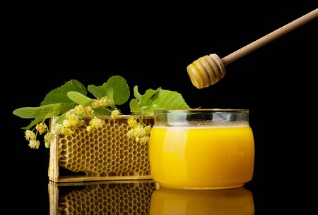 Jar of fresh honey, spoon and a sprig of linden, isolated on black backgroundの写真素材