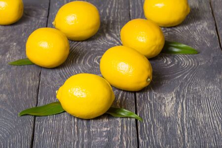 On grey wooden surface large yellow lemons with leavesの写真素材