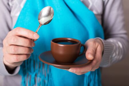 Cup of fragrant morning coffee and teaspoon in hands of womanの写真素材