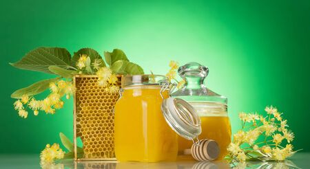 Banks with honey, honeycomb, wooden spindle and Linden flowers on green backgroundの写真素材