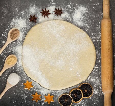 Dough layer on surface sprinkled with flour, rolling pin, dried citrus and spices in spoonsの写真素材