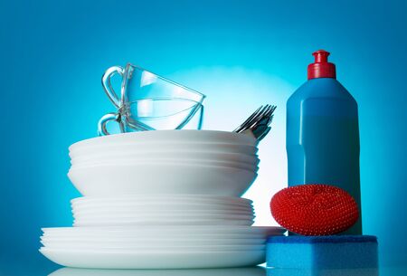 Clean plates, Cutlery and cups, near detergent and sponge, on blue backgroundの写真素材