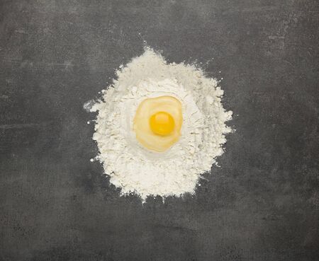 Handful of flour, egg on top, on gray work surfaceの写真素材