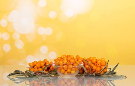 A bowl of ripe berries of sea buckthorn branch with berries and leaves on abstract yellow background.の写真素材