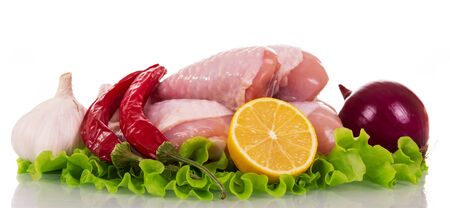Raw chicken legs, onion, hot pepper, garlic, part of lemon and lettuce leaves isolated on white background.の写真素材