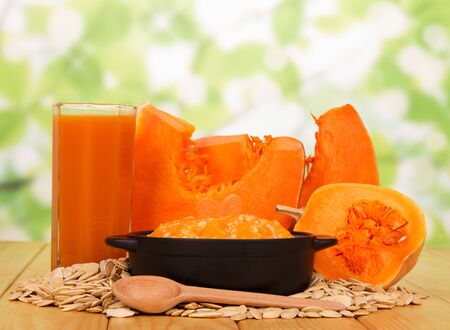 Pieces of different pumpkins, a glass of pumpkin juice, porridge in a saucepan, pumpkin seeds and a wooden spoon on an abstract green background.の写真素材