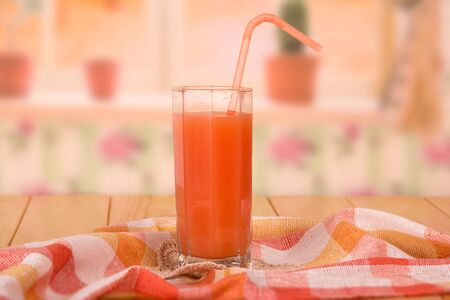 A glass of fresh grapefruit juice with a straw, towel, and lace napkin on kitchen background.の写真素材