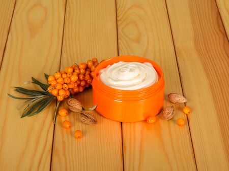 A branch with sea-buckthorn berries, a jar of cream and almond bones next to a light wood background.の写真素材
