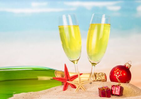Bottle and two glasses of champagne, Christmas ball, gifts, and starfish in the sand against the sea.の写真素材
