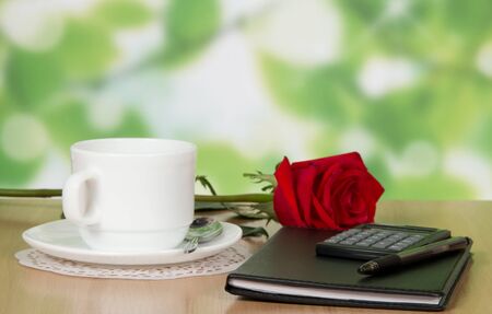 Office accessories, cup and saucer and a red rose on the tableの写真素材