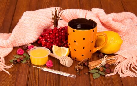 A cup of tea for colds, viburnum, lemon and a warm scarf on the tableの写真素材