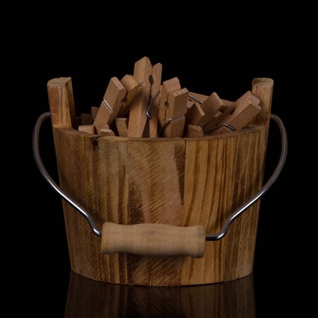 Wooden bucket full of clothespins isolated on black backgroundの写真素材
