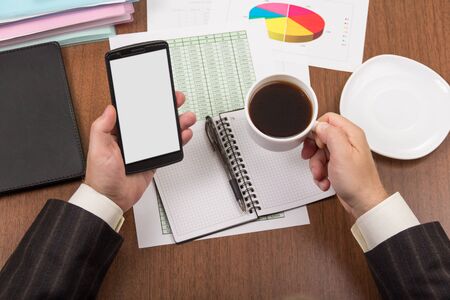 Office table with accessories, folders and documents, cup of coffee in  male's handの写真素材