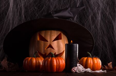 Halloween pumpkin head jack lantern with big black witch hat on the background of cobwebsの写真素材