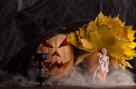 Pumpkin Halloween with a black cap and autumn leaves against the backdrop of a cobwebの写真素材