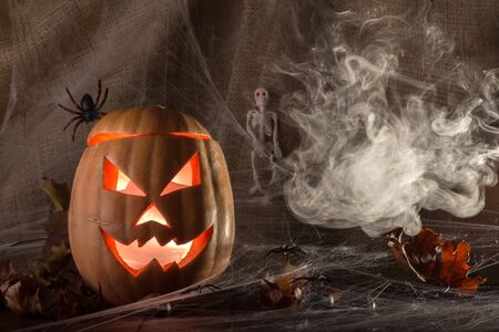 Halloween concept. The ghastly, ghastly pumpkin glows with a fiery yellow light smoke and autumn leavesの写真素材