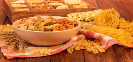 A bowl of farfalle, a bunch of spaghetti, nest of thin vermicelli, noodles and a box with various pasta on a red background.の写真素材