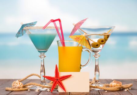 Cocktail, a glass of orange juice and alcohol with olives, a blank card, a starfish, seashells and twine on the background of the sea.の写真素材