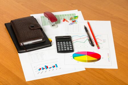 Calculator, pen, notebooks, sheets of paper with the accounts and diagrams, other stationery on the desktop background.の写真素材