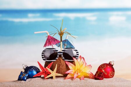 Coconut with sunglasses, starfish and Christmas balls, gifts in the sand against the seaの写真素材