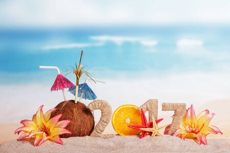 Inscription 2017 decorated Christmas coconut, orange and tropical flowers in the sand on background of oceanの写真素材
