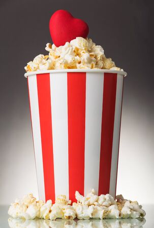 Red heart in a bright paper box with popcorn on a gray backgroundの写真素材