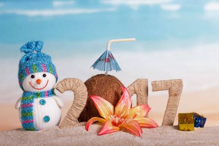 The inscription 2017 in the sand, a snowman, a Christmas ball on the background of the oceanの写真素材