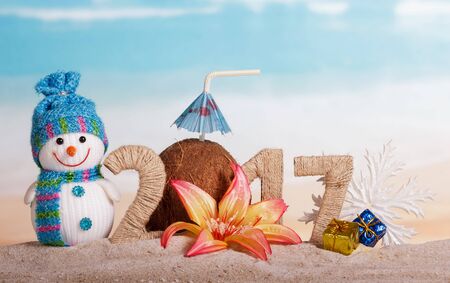Christmas snowman, coconut and the inscription 2017 in the sand, decorated with a flower and gifts on the background of the seaの写真素材