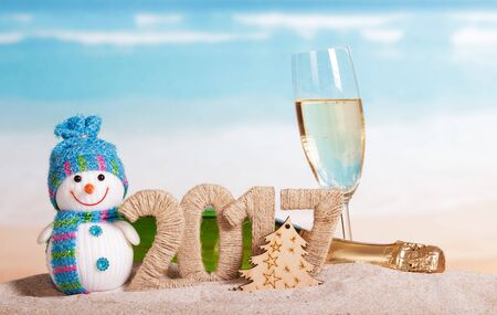 Christmas 2017 inscription, champagne, snowman in the sand on background of oceanの写真素材
