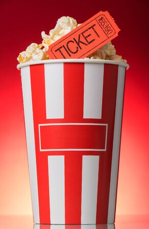 Large striped popcorn box with orange a ticket to the movies on a bright red backgroundの写真素材
