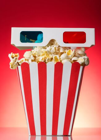 The square striped box with popcorn and 3D glasses on a red backgroundの写真素材