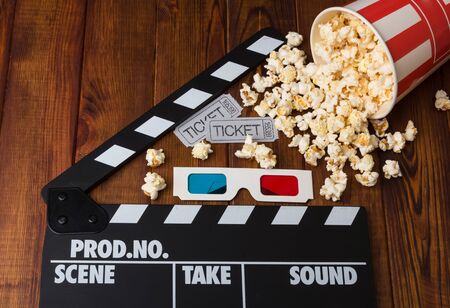 Movie tickets, 3D glasses, paper box spilled popcorn and movie clapper on a wooden backgroundの写真素材