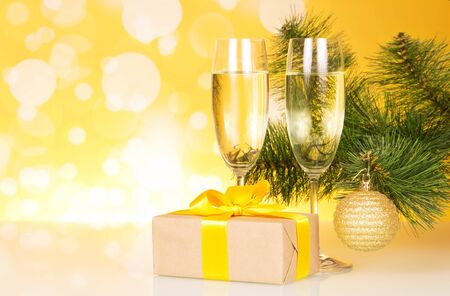 Glasses of champagne, Christmas gift and Christmas tree on a yellow backgroundの写真素材