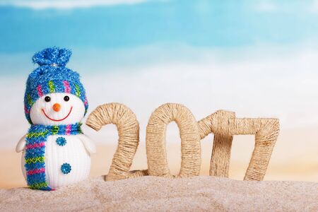 The inscription 2017 in the sand and a snowman on the background of the seaの写真素材