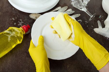 Women's hands in gloves wash dishes with detergent, on black backgroundの写真素材