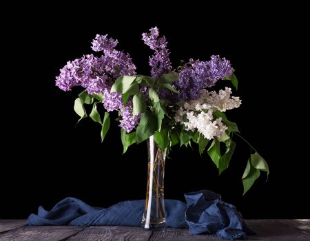 A bouquet of purple and white lilac stands in glass vase, isolated on black backgroundの写真素材
