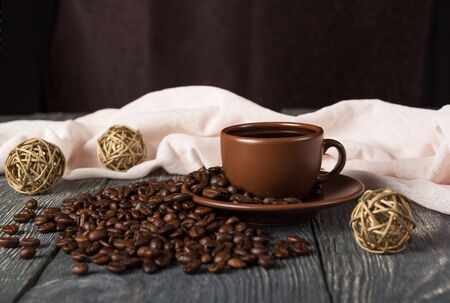 Cup of coffee with saucer on scattered grains, balls of rope, next to light fabric, on wooden surfaceの写真素材