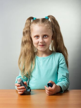 Smiling little girl sitting at table with an inhaler in her handの写真素材