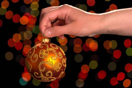 Female hand holding beautiful Christmas ball toy, shimmering on dark backgroundの写真素材