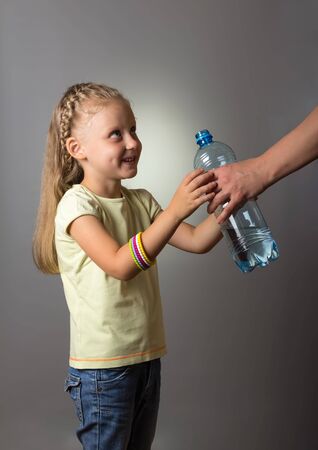 Little smiling girl takes water bottle from hands of an adult on gray backgroundの写真素材