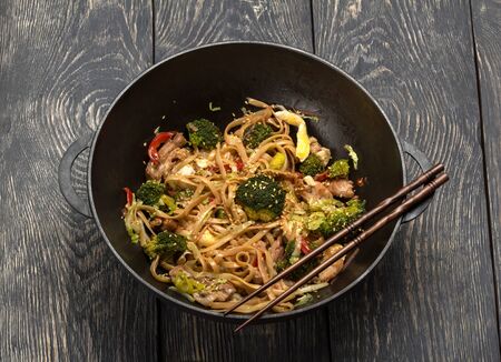 Asian dish of meat, vegetables and noodles with spices in wok, on background of wooden tableの写真素材