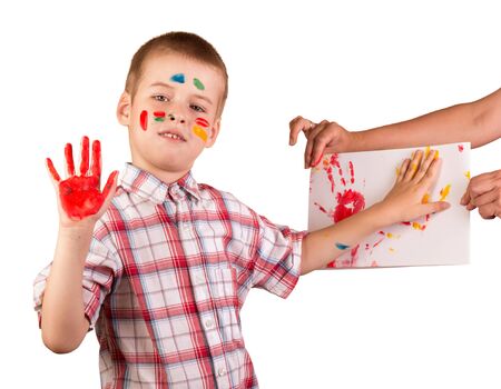 Boy draws finger paints on sheet of paper, his face and hands in the paint isolated on white backgroundの写真素材
