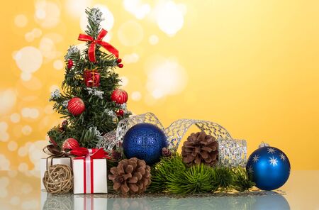 Little beautifully decorated Christmas tree, gifts, cones, toy-balloons, on light yellow backgroundの写真素材