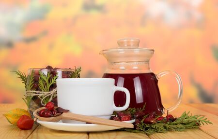 Jug with of broth hips, dried berries in jar and spoon, on wooden tableの写真素材