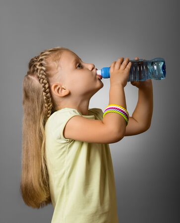 Adorable little girl drinking fresh clean water from plastic bottle on grey backgroundの写真素材